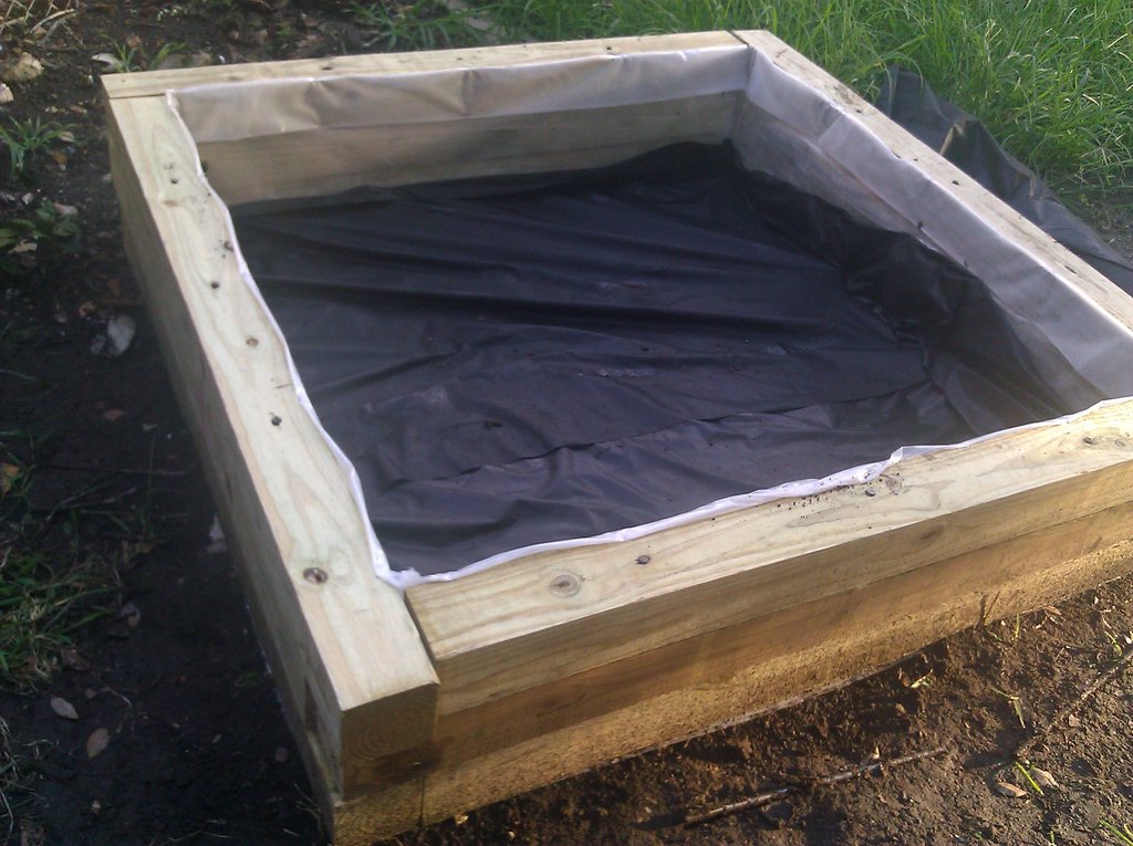 The plastic wrap was placed only on the sides to keep the pressure-treated wood (good for elements, bad for plants) from seeping into the soil. Landscape fabric (black tarp) allows water to drain freely while keeping weeds from using my good soil.